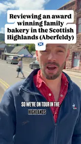 Two creators visit Breadalbane Bakery in Aberfeldy, Scotland, to review their baked goods. They purchase a fruit slice and a donut, providing commentary on the taste and value while walking around the town.