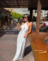 A lifestyle-focused promotional shot featuring a creator posing on an outdoor terrace at a Greek restaurant, highlighting the venue as a summer dining destination.