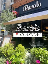 A bright, eye-level exterior shot of Barolo restaurant in Glasgow, featuring the signage, outdoor seating area, and floral decorations.
