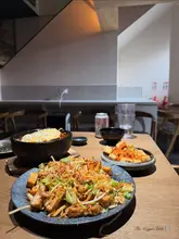 A casual, top-down shot of a table filled with various Asian-inspired vegetarian dishes, including noodles, bibimbap, and small plates, captured in a restaurant setting.