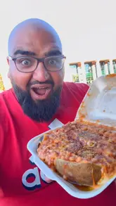 A creator reviews a jacket potato from the Spud Bros food truck, highlighting the long queue, the preparation process, and the final taste test of a loaded jacket potato with cheese, beans, crispy onions, and garlic chicken.