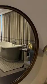 A photo taken through a circular mirror showing a hotel room with a freestanding bathtub, highlighting the elegant and homely interior of a Georgian Deluxe room at a hotel in Richmond.