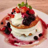 A close-up, eye-level shot of a stack of pancakes topped with fresh berries, blueberry compote, and crème fraîche, served at The Table Cafe.