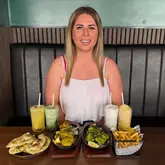 A photo of a person sitting at a restaurant table featuring a spread of Indian-fusion dishes including sizzler plates, fries, and various drinks.