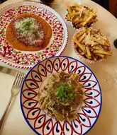 A high-quality, overhead flat-lay photograph of an Italian meal featuring chicken milanese, truffle pasta, and parmesan fries, served on vibrant, decorative ceramic plates.