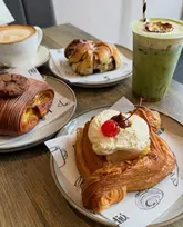 A high-quality, well-lit photograph of an assortment of artisan pastries and a matcha drink on a wooden table, showcasing the bakery's fresh offerings.