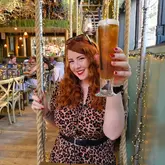 A portrait of a woman holding a glass of beer in a warm, ambiently lit restaurant or bar setting, used to accompany a personal reflection on social media authenticity.