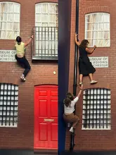 A split-screen image showing two people interacting with an optical illusion exhibit at the Museum of Illusions in Manchester, where the perspective makes it appear as though they are climbing the side of a building.