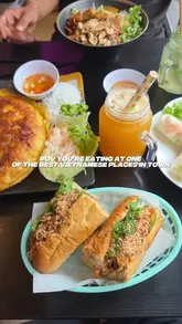 A vibrant, overhead flat-lay shot of a Vietnamese meal featuring banh mi, banh xeo, and drinks, effectively showcasing the variety and freshness of the food in a casual dining setting.