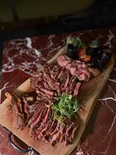 A high-quality, moody, and atmospheric shot of a large sharing steak platter served on a wooden board, showcasing the premium nature of the venue's dry-aged meat selection.