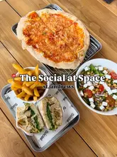 A bright, overhead flat-lay shot of a casual lunch spread featuring a pizza, a sandwich with fries, and a salad, captured at The Social at Space in St. Andrews.