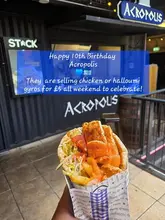 A handheld, first-person perspective shot of a gyros wrap held in front of a street food stall, featuring a prominent blue text overlay announcing a 10th-anniversary promotion.