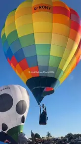 A bright, high-quality photograph capturing a colourful hot air balloon ascending into a clear blue sky at the Bristol Balloon Fiesta.