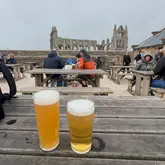 A casual, eye-level shot of two glasses of beer on a weathered wooden table at an outdoor venue, with the ruins of Whitby Abbey visible in the background.