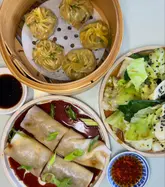 A high-quality, overhead food photography shot showcasing a variety of Chinese dishes, including steamed dumplings, beef cheung fun, and stir-fried greens. The lighting is bright and even, highlighting the textures and colors of the food, making for an appealing and professional-looking social media post.