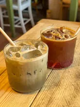 A clean, well-composed shot of two iced drinks served in simple glassware on a rustic wooden table, capturing a relaxed, countryside cafe atmosphere.
