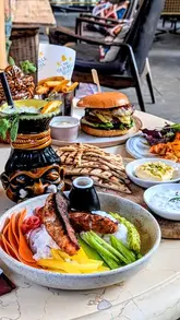 A promotional video showcasing the 'Tiki Bar' pop-up at The Old Bell Hotel, featuring various dishes like poke bowls, burgers, and skewers, alongside themed cocktails in a tropical-inspired setting.