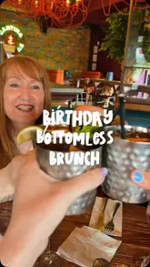 A casual, first-person perspective shot of a birthday bottomless brunch celebration at a restaurant, featuring a cheers with cocktails.