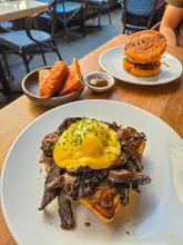 A high-quality, well-lit shot of a brunch spread at a restaurant, featuring a prominent dish of wild mushrooms on toast topped with hollandaise, alongside other brunch items.