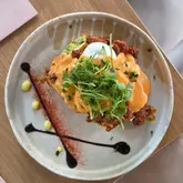 A top-down, overhead shot of a brunch dish featuring a cajun chicken stack with poached eggs, avocado, and microgreens, served on a ceramic plate with a balsamic glaze garnish.