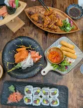 A high-quality, overhead flat-lay photograph showcasing a variety of Japanese dishes including sushi rolls, salmon sashimi, spring rolls, and fried chicken, served on a wooden table at Miso House in Sunderland.