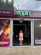 A casual, bright photo of a child standing in the entrance of a Tenpin bowling alley, showcasing the venue's branding and signage.