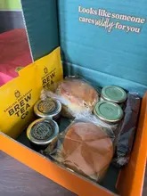 A top-down shot of an afternoon tea delivery box containing scones, jam, tea bags, and a brownie, all in their original packaging.