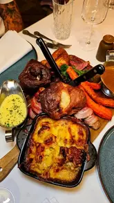 A promotional reel for The Grand Hotel in Swansea, highlighting their new 'Fondue Dipping Roast'. The video features close-up shots of the roast dinner components, including braised beef, Yorkshire puddings, and dipping sauces, followed by dessert. The creator is shown enjoying the meal and wine in the venue.