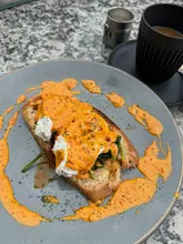 An overhead, natural-light shot of an Nduja Eggs Benedict dish served with a coffee, captured on an outdoor table.