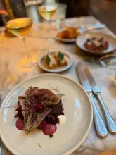 A high-quality, atmospheric shot of a fine dining spread at The Spence in Edinburgh, featuring a beautifully plated main dish in the foreground with drinks and other courses softly blurred in the background.