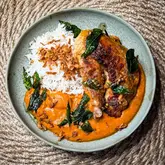 A high-quality, overhead shot of a home-cooked meal featuring spatchcock tandoori guinea fowl served with a vibrant, south-Indian style curry leaf gravy and basmati rice, garnished with crispy onions and fried curry leaves.