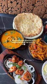 A promotional video for an Indian restaurant featuring a montage of dishes including curry, naan, rice, and chicken tikka, alongside cocktail shots and interior views of the venue. The creator appears in the video, and the edit is set to music with text overlays.
