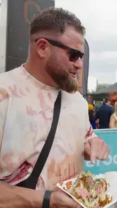 Two creators review chicken wings from the 'Ginger Wings' stall at Wing Fest London, providing commentary on the flavors and textures of the 'Buffalo' and 'Wild' wings.