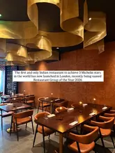 A professional, wide-angle interior shot of a high-end restaurant dining room, featuring warm ambient lighting, modern decor with gold ceiling accents, and precisely set tables, conveying an atmosphere of luxury and exclusivity.