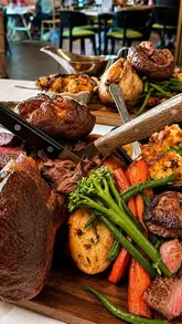 A montage video showcasing a Sunday roast dining experience at The Grand Hotel in Swansea, featuring close-ups of a large sharing platter, gravy pouring, and desserts.