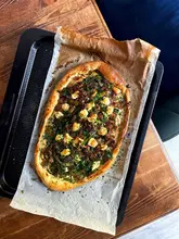 A rustic, homemade pastry tart topped with sausage meat, red onion, broccoli, asparagus, and brie, captured from an overhead angle on a wooden surface.