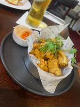 A casual, top-down shot of a calamari starter served in a metal basket with branded paper, accompanied by a drink, at a Miller & Carter restaurant.