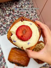 A high-quality, close-up shot of a creative pastry held in hand, showcasing excellent lamination and fresh ingredients. The background features a trendy terrazzo surface with other pastries, creating a cohesive and appealing aesthetic for a bakery.