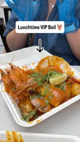 Two creators visit a seafood market stall, 'Rock & Scallop', to review their lunch offerings, specifically the VIP Surf and Turf and the Lunchtime VIP Seafood Boil. The video features the creators talking to the camera, showing the menu, and enjoying the food.