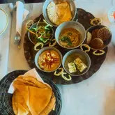 A top-down, overhead shot of a Middle Eastern breakfast platter featuring various small bowls of dips, falafel, and eggs, served with a basket of flatbread.