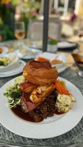 A montage showcasing a Sunday lunch experience at The Stables at Beamish Hall, featuring a prawn cocktail starter, a large mixed meat roast dinner, and a lemon and blackcurrant dessert, along with shots of the venue's exterior and courtyard.