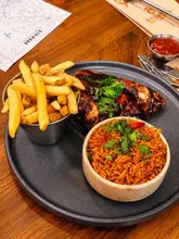 A top-down shot of a meal consisting of grilled chicken, fries, and rice, served on a dark plate.