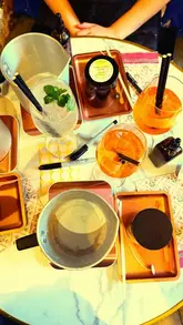 A montage video showing a group of friends participating in a candle-making workshop at a venue, interspersed with shots of them enjoying cocktails.
