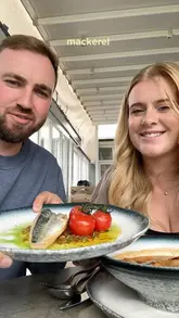 A couple visits the Upper Deck restaurant at the Christchurch Harbour Hotel for a lunch date, participating in a 'we order for each other' challenge. They showcase several dishes including bouillabaisse, mackerel, lamb, chicken with prawns, and desserts, while discussing their experience.