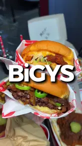 A fast-paced food review video featuring a creator trying various Nashville-style chicken dishes, burgers, and sides at a venue called BiGYS. The video uses a vlog-style format with voiceover commentary to guide the viewer through the menu items, highlighting the cheese pull and specific dishes.