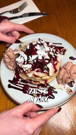 ZEST, YORK 🥑 INVITE | There’s a new brunch spot in York, and when we were invited down, we had to give it a try. Located just off Whip-Ma-Whop-Ma-Gate (possibly the best-named street), @Zest York  is a Mediterranean-inspired restaurant serving brunch, dinner, and cocktails. We ordered: 🥓 The Breakfast Tower — Cumberland sausage, bacon rashers, poached egg, grilled tomato, sourdough bread, chilli jam (£10.95) 🫒 Mediterranean Breakfast — Turkish paçanga, poached eggs, olives, feta, pitta bread, honey (£12.95) 🧋 Wild berries & tropical smoothies (£6.95) The restaurant had a great atmosphere and was already busy, always a good sign. We also noticed some excellent offers, including a free hot drink with brunch and 2-for-1 smoothies, which we happily took advantage of. The latte was a standout; we enjoyed it so much we ordered another. Amber chose the Mediterranean Breakfast—it was light and enjoyable, though probably not something she’d order again. The clear winner, however, was the Breakfast Tower. The chilli jam really elevated the dish and made it the standout plate of the morning.