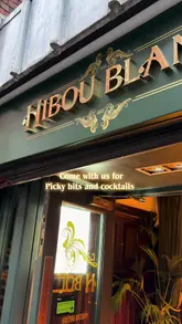 A short, handheld montage showcasing the interior and food offerings at Hibou Blanc. The video features shots of the venue's decor, including a chandelier, followed by close-ups of chicken strips and fries, and a shot of the bar's liquor selection.