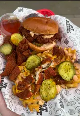 A creator reviews a special Ramadan box meal at Hot Birdies, showcasing the Nashville hot chicken burger, loaded waffle fries, and a date, while highlighting the value and quality of the food.