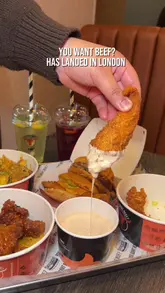 A short, energetic promotional video for a new burger restaurant in London called 'You Want Beef?'. The video features quick cuts of various menu items, including smash burgers, loaded fries, chicken wings, and mojitos, alongside shots of the venue's interior and menu board.