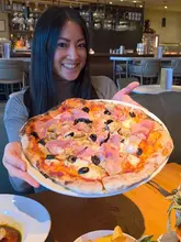 The video features a creator visiting Fiume, an Italian restaurant at Battersea Power Station. It highlights various dishes including veal carpaccio, pizza, pasta, sea bass, and tiramisu, while also showcasing the restaurant's interior, pizza oven, and riverside location.